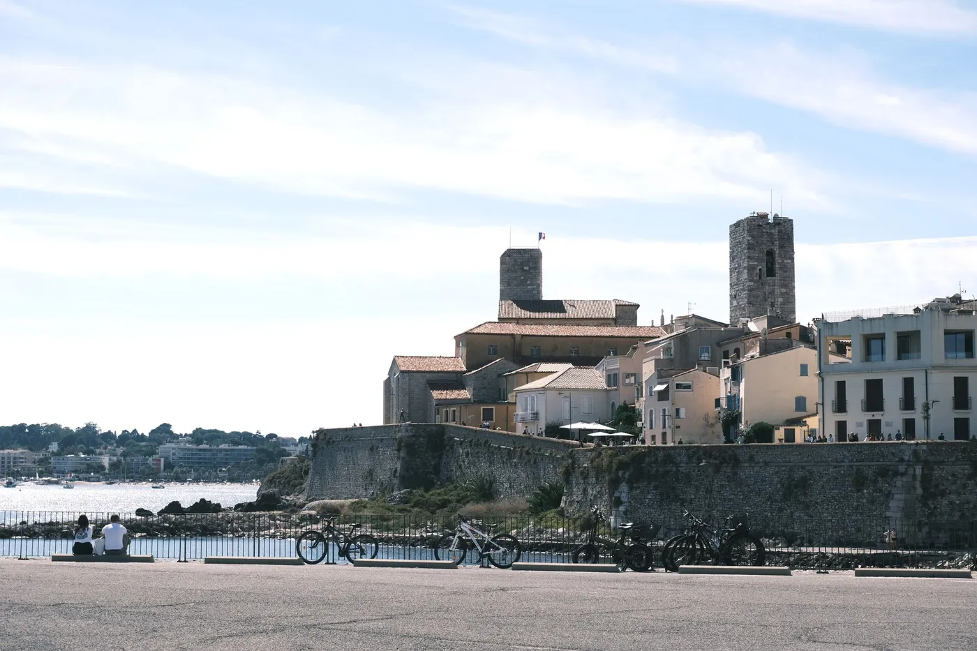 View of historic Antibes with prominent fort tower by the sea, bicycles in foreground.