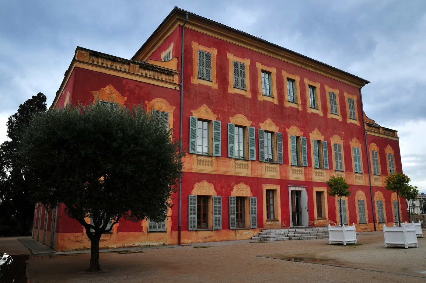 The red exterior facade of the Musee Matisse in Nice, with olive trees.